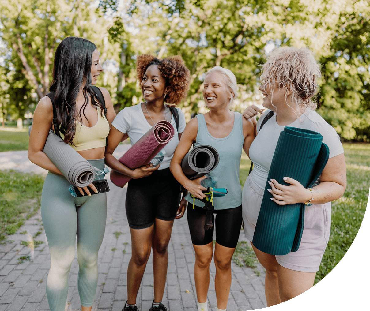 Smiling women holding exercise mats outdoors